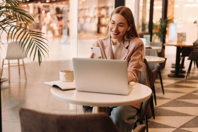 A millennial business woman works and studies online using a mobile phone and technology in a cafe