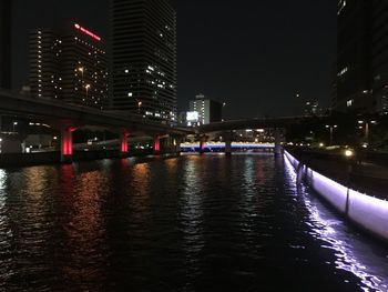 Illuminated bridge over river by buildings in city at night