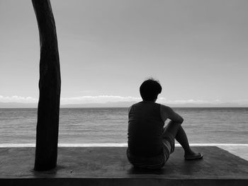 Rear view of man sitting on beach against sky