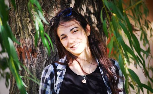 Smiling young woman against tree trunk