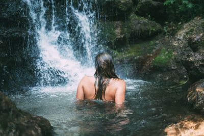 Rear view of topless woman enjoying waterfall in forest