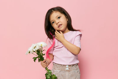 Portrait of young woman holding flowers against pink background
