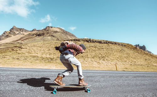 Side view of man skateboarding on road against sky