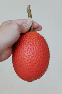 Close-up of hand holding strawberry over white background