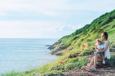 Side view of woman sitting on field against sky