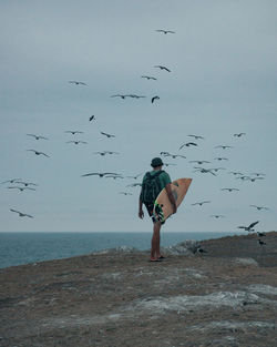 Full length of man walking while holding surfboard by sea