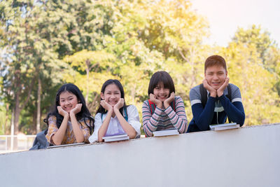 Portrait of smiling friends standing by retaining wall