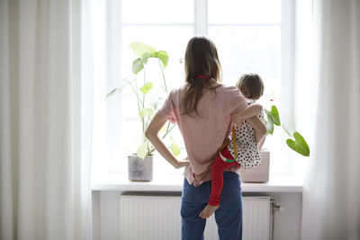 Rear view of fashion designer carrying daughter while standing at home