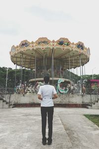 Rear view of boy at amusement park against sky