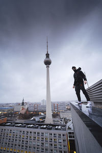Low angle view of young man standing on building against cloudy sky