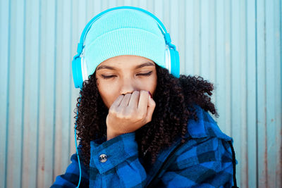Young woman listening to music on headphones against closed shutter