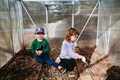 Young brother and sister digging up plants from backyard greenhouse