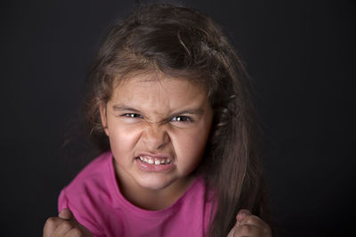 Portrait of angry girl clenching teeth against black background