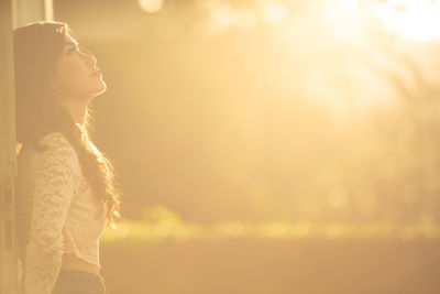 Side view of woman looking away against sky during sunset