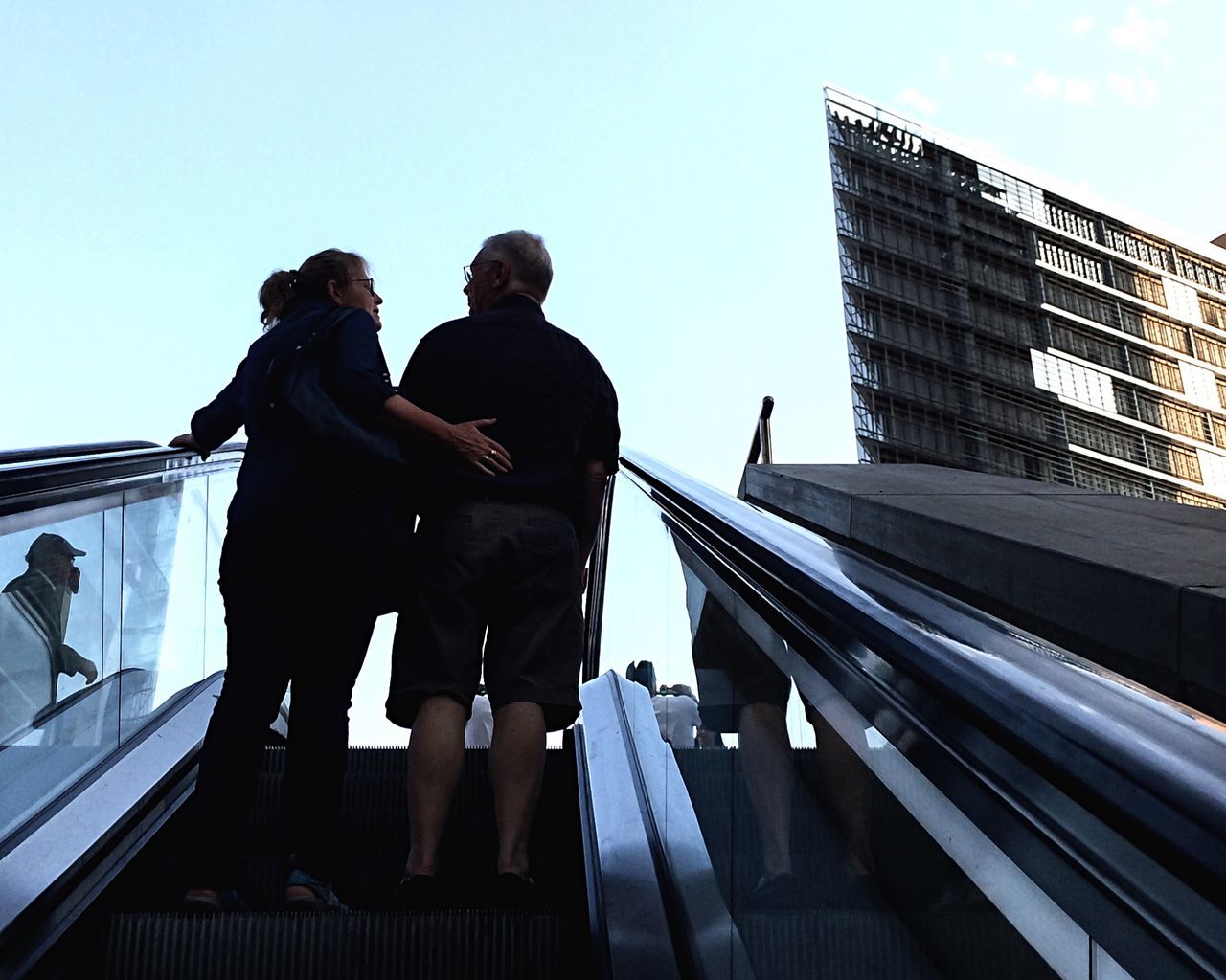 architecture, built structure, men, building exterior, lifestyles, low angle view, clear sky, railing, city, leisure activity, person, standing, sky, city life, full length, walking, day