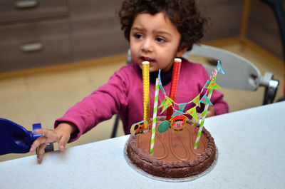 High angle view of girl sitting by birthday cake on table at home