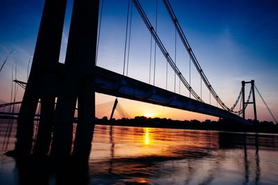 Silhouette bridge over river during sunset
