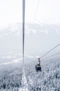 Overhead cable car on snow covered landscape against sky