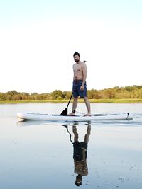 Full length of shirtless man standing in water against sky