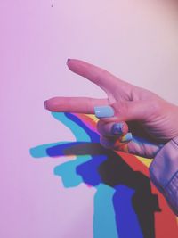 Cropped hand of woman gesturing peace sign against wall