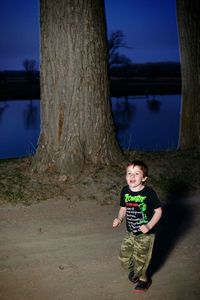Full length of smiling boy on tree trunk at night