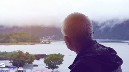 Rear view of man by lake against mountains and sky