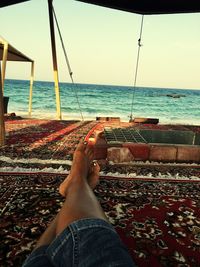 Low section of woman relaxing on beach against sky