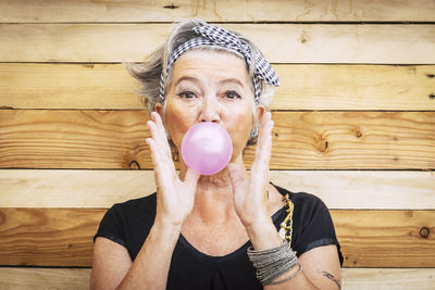 Portrait of senior woman blowing bubble gum against wooden wall