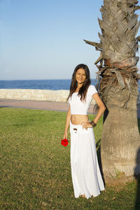 Portrait of young woman standing on field by sea