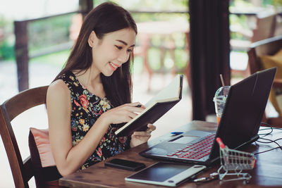 Businesswoman reading book while using laptop in cafe