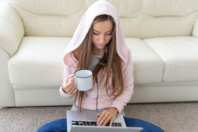 Young woman using phone while sitting on sofa at home