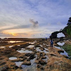 Rear view of people walking on beach against sky during sunset