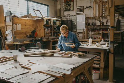 Senior female carpenter holding frame while working at workshop