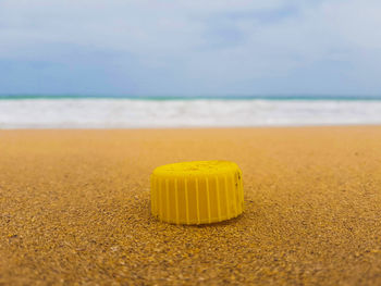 Yellow plastic bottle cap on beach against sky