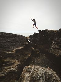 Side view of man on rock against sky