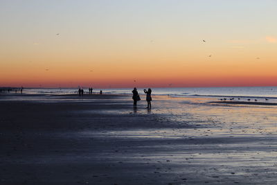 Silhouette people on beach against sky during sunset