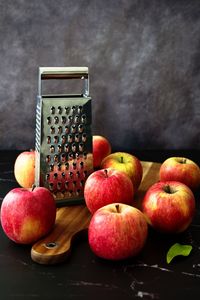 Red apples and grater on wooden cutting board against black background