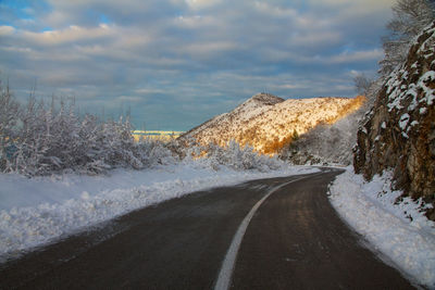 Road amidst snow covered landscape against sky