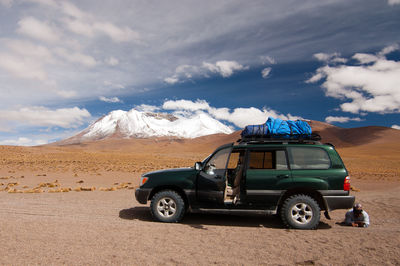 Off-road vehicle on field against cloudy sky