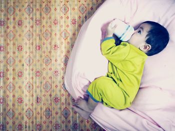 Cute boy drinking milk from bottle while lying on bed