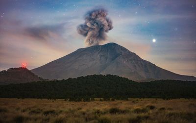 Scenic view of erupting volcanic mountain against sky during sunset