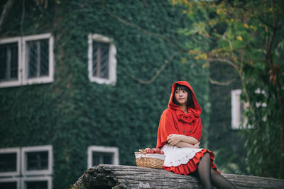 Woman sitting on wood against trees