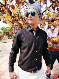 Young man looking away while standing by tree