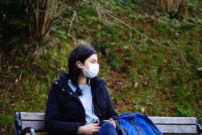 Young woman wearing mask sitting on bench