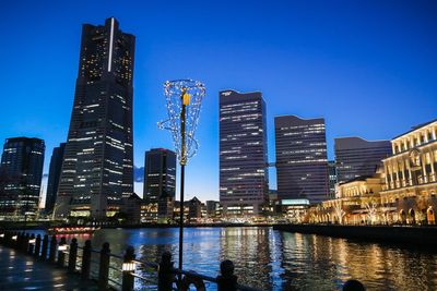 Illuminated buildings in city against clear blue sky