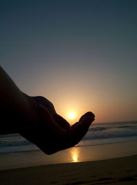 Close-up of silhouette hand against sea at sunset