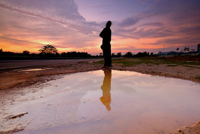 Silhouette man standing on riverbank against sky during sunset