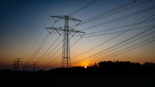 Low angle view of silhouette electricity pylons on field against sky at sunset