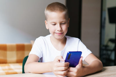 Happy cute baby, kid, son sitting at table relaxing, having fun with mobile