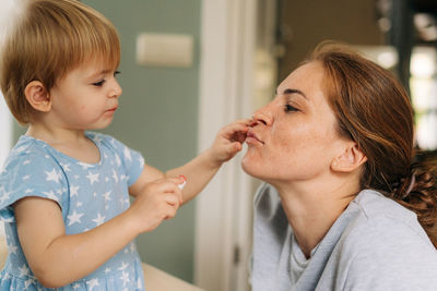 A little daughter makes a make-up for her mother and paints her lips with lipstick.